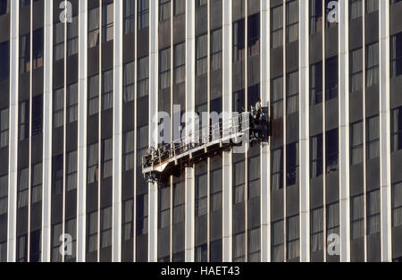 Fearless window cleaners work high above the ground from a suspended scaffold that is a movable platform known as a swing stage which descends on wire ropes from the roof of a high-rise building in Los Angeles, California, USA. Washing windows on skyscrapers has long been considered a dangerous occupation although the number of high-rise window-cleaner deaths or injuries is statistically very low according to the International Window Cleaning Association. Stock Photo