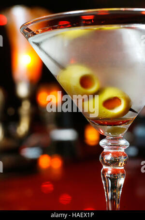 A martini with olives sits on a bar in a cocktail lounge.