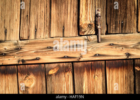 Rusty metal hinge on aged faded wood in brown. Vertical composition of fading timber and a door entrance opening. Stock Photo