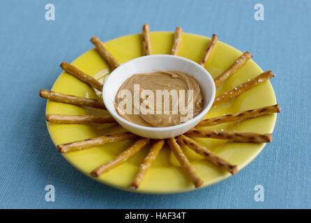 Pretzel sticks on a yellow plate surrounding peanut butter. Stock Photo