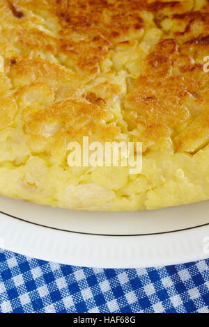 Spanish potato omelette detail on a dish and blue tablecloth. Vertical Stock Photo