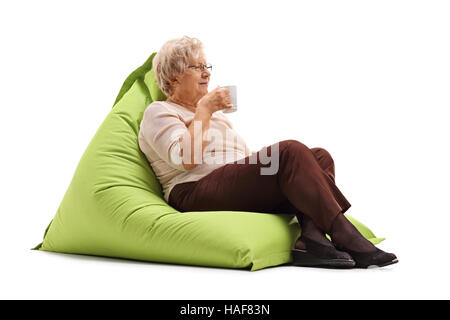 Elderly woman sitting on a beanbag and holding a cup isolated on white background Stock Photo