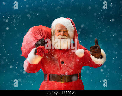 Happy Santa Claus gesturing thumb up with big bag full of gifts to children. Merry Christmas & New Year's Eve concept. Stock Photo