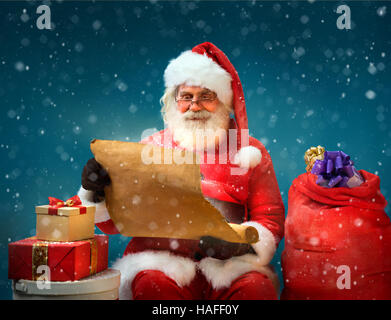 True Santa Claus reads long list of gifts for children on blue background. Merry Christmas & New Year's Eve concept. Stock Photo