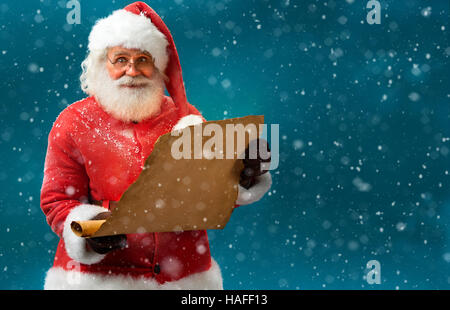 Happy Santa Claus holding vintage paper on blue background. Merry Christmas & New Year's Eve concept. Stock Photo