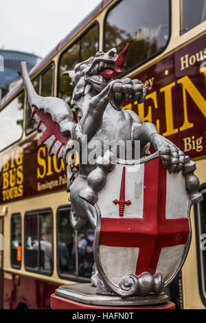 A silver statue captured in front of a tourist bus as it begins to pass over London Bridge in London.