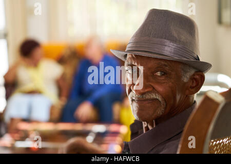 Portrait of elderly black man looking at camera in retirement home, with group of friends in background. Patients relaxing in hospice for seniors. Stock Photo