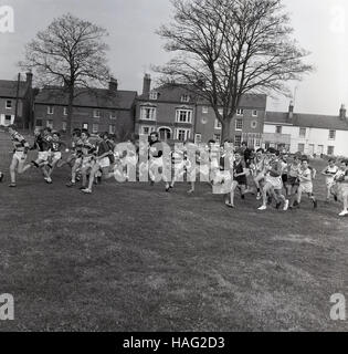 1965, historical, group of young school children set off on a cross-country running race from a village green. Stock Photo