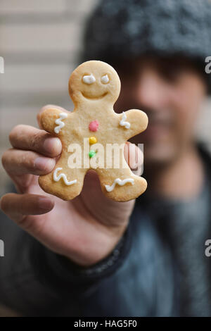 closeup of a young caucasian man wearing a knitted cap holding a gingerbread man in his hand in front of his face Stock Photo
