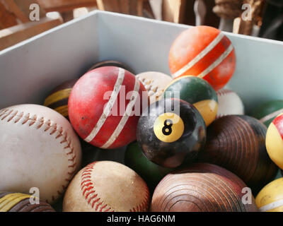 An old eight ball in wooden bin full of vintage game balls, including pool, croquet, and baseball. Stock Photo