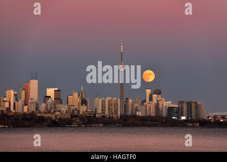 The rising full moon and Toronto skyline are lit by the setting sun on ...