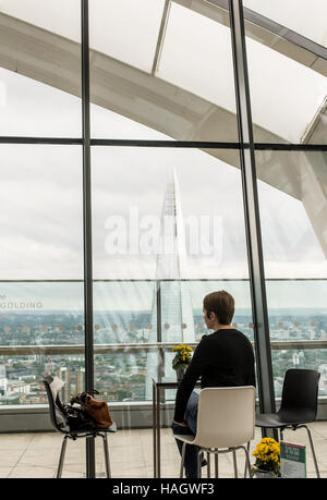 Woman alone sitting at a table in a cool bar enjoying the spectacular view of the Shard from the Sky Garden Stock Photo