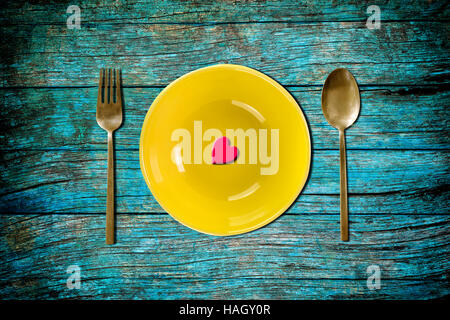 red heart shape on yellow empty plate with fork and spoon on blue vintage wooden table for love dinner concept Stock Photo