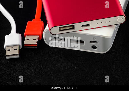 Red and white power bank with usb cable on black leather background. Stock Photo