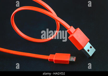 Orange color USB cable on black leather background. Stock Photo
