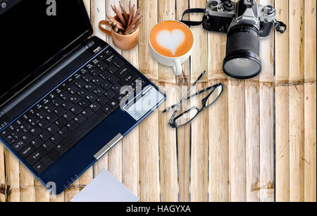 Bamboo desktop with notebook, vintage camera, cup of coffee and eyeglasses. Stock Photo