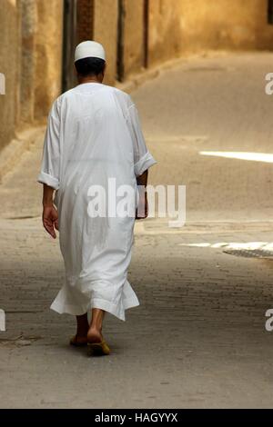 Muslim male dressed in traditional white djellaba walks in an alleyway in the old town of Fez, Morocco. Stock Photo