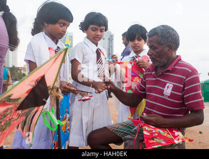 School children watch a man making kites ,Galle Face Green,Colombo,Sri Lanka. Stock Photo