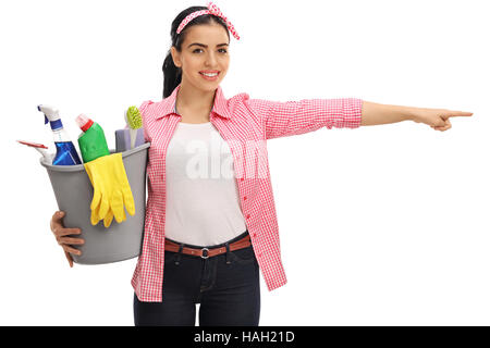 Happy woman holding a bucket filled with cleaning products and pointing right isolated on white background Stock Photo