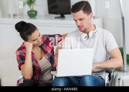 disabled man using laptop sitting next to his girlfriend Stock Photo