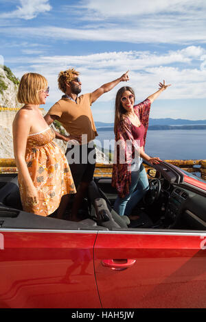 Group of happy young people waving and pointing fingers from the red convertible. Stock Photo