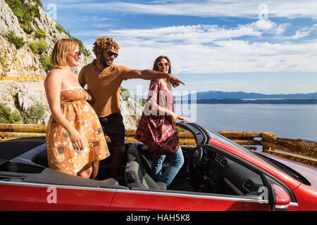 Group of happy young people waving and pointing fingers from the red convertible. Stock Photo