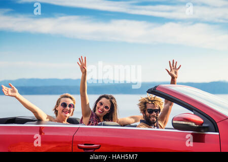 Group of happy young people waving from the red convertible. Stock Photo