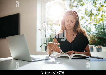 Young woman studying at home. Young woman sitting at table with laptop reading book. Stock Photo