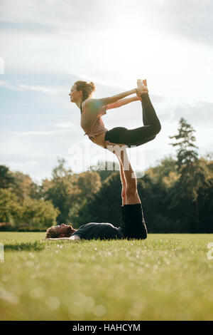 Flexible and strong young couple doing acroyoga outdoors. Man and woman in park practising pair yoga poses. Stock Photo