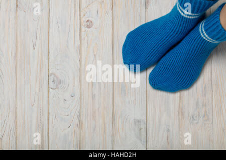 Female feet in knitted blue socks on white wooden background. Stock Photo