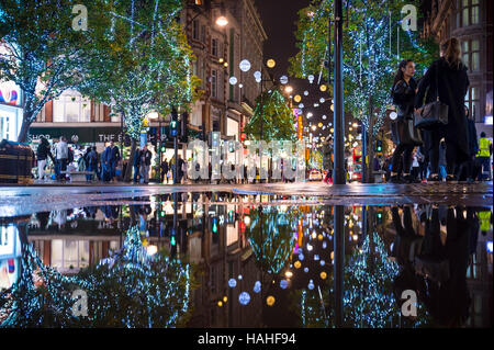LONDON - NOVEMBER 16, 2016: Holiday lights twinkle in a puddle reflection as pedestrians crowd the sidewalks of Oxford Street. Stock Photo