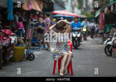 Young asian woman is sitting on a chair in the middle of a bustling street. Stock Photo