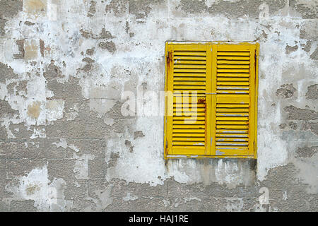 closed yellow wooden window shutters on the old stone wall Stock Photo