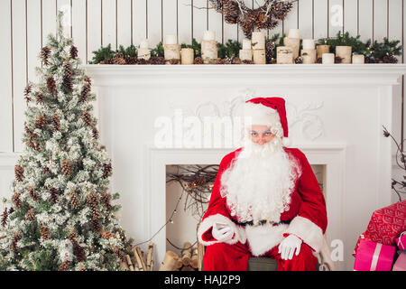 Grumpy Santa leaning exhausted on his office desk with mobile phone Stock Photo