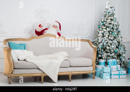 Santa Claus hiding behind a sofa over home interior Stock Photo