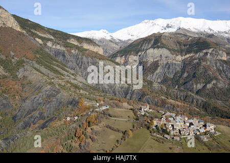 AERIAL VIEW. Medieval hilltop village in a landscape of badlands and snow-covered peaks. Chateauneuf d'Entraunes, Alpes-Maritimes, France. Stock Photo