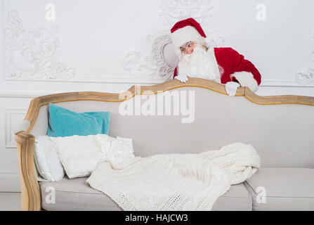 Santa Claus hiding behind a sofa over home interior Stock Photo