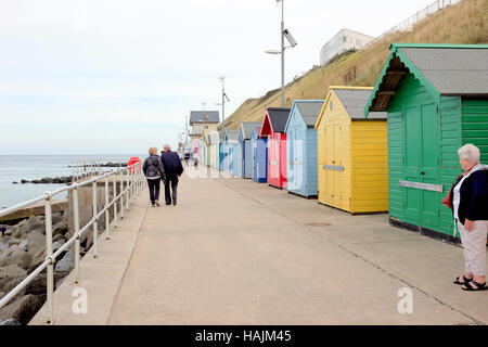 Sheringham, Norfolk, UK. September 24, 2016.  Holidaymakers walking the promenade passing colorful beach huts on the seafront . Stock Photo