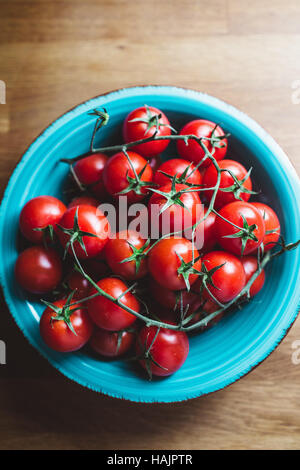 Cherry tomatoes on the vine. Blue bowl of cherry tomatoes on wooden table. Stock Photo
