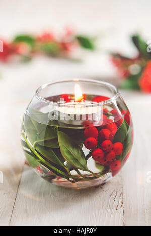 Christmas Table Decoration. Glass vase with holly berries and white floating candle. Stock Photo