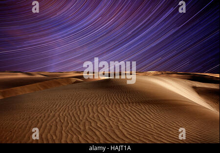 Night in the desert sand dunes and star trails on blue night sky Stock Photo