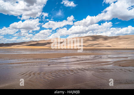 Springtime at Great Sand Dunes - White clouds, on blue sky, passing over rolling sand dunes and gently flowing Medano Creek. Stock Photo