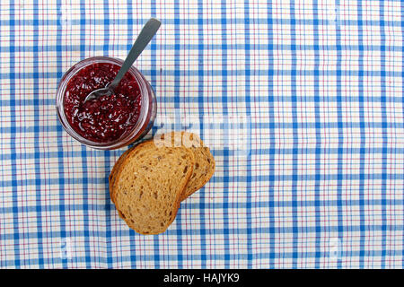 jar with raspberry jam and sliced bread on blue tablecloth Stock Photo