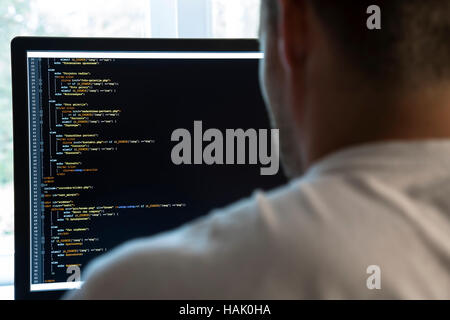 programmer from behind and programming code on computer monitor. focus on monitor Stock Photo