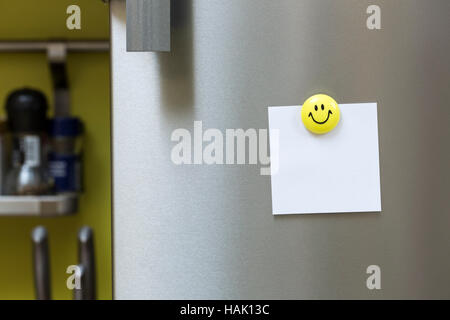 blank paper note with magnet hanging on fridge door Stock Photo