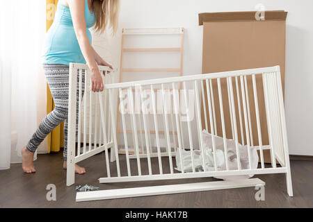 young pregnant woman assembling bed for expectant baby Stock Photo