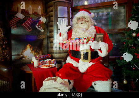 Santa in grotto christmas display   lighted christmas tree, presents,fireplace,stockings gifted wrapped reading costume good sack red in pub Santa Cla Stock Photo