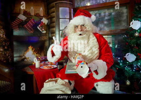 Santa in grotto christmas display   lighted christmas tree, presents,fireplace,stockings gifted wrapped reading costume good sack red in pub Santa Cla Stock Photo