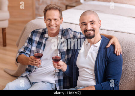Delighted gay couple drinking wine in the bedroom Stock Photo