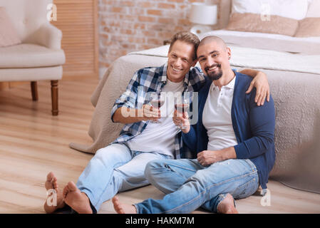 Smiling homosexual couple drinking wine in the bedroom Stock Photo